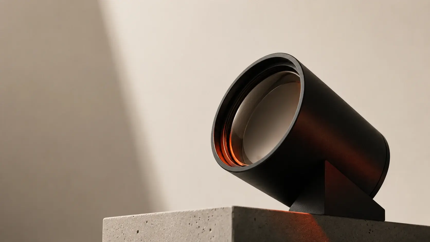 Ein schwarzer Scheinwerfer auf einem Betonsockel richtet sich nach vorn; in der Linse glüht warmes Orange, dahinter fällt ein heller Lichtstreifen auf eine cremefarbene Wand.